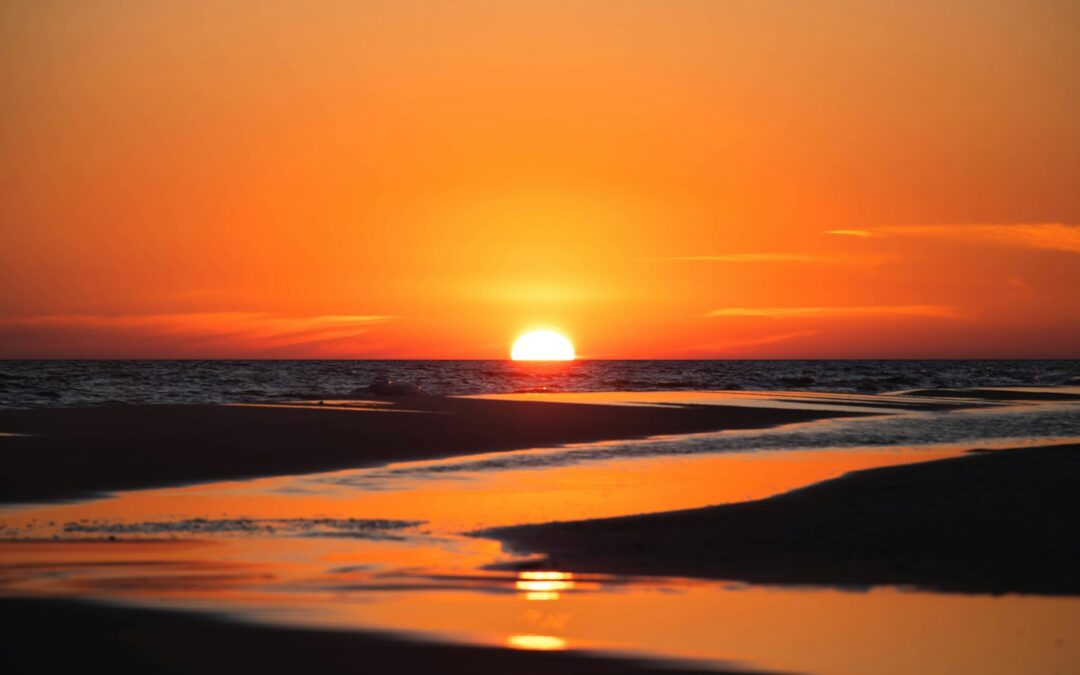 the sun is setting over the ocean on a beach